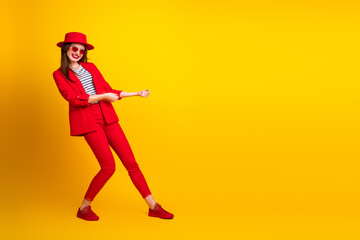 Fashionable young woman in stylish red suit posing against vibrant yellow background with confident gesture