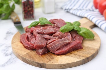 Fototapeta premium Pieces of raw beef meat, basil and ingredients on white marble table, closeup