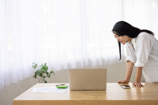 Woman Leaning Over Desk to Look at Laptop Screen