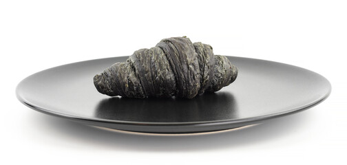Black charcoal croissant with black plate on a light background