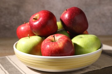 Fresh red and green apples in bowl on wooden table against grey background, closeup