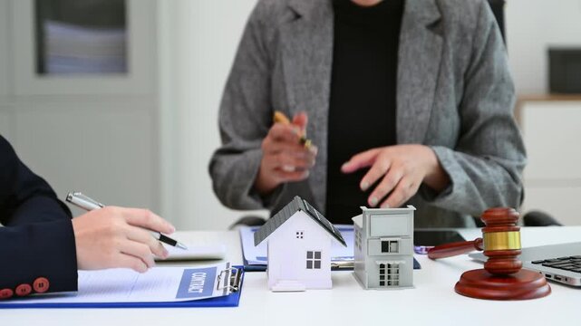 Two professionals reviewing real estate documents with house models and a gavel showing property contract consultation legal advice negotiation