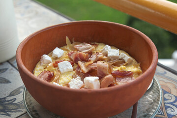 A traditional Hutsul Ukrainian dish made from creamy corn porridge, topped with fried bacon, caramelized onions, and soft white cheese, served in a rustic clay bowl with authentic homemade flavor.