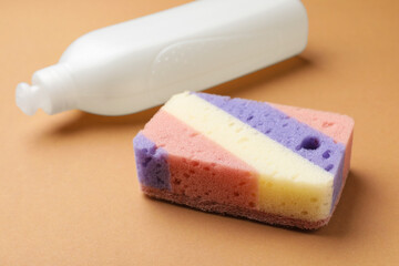 Kitchen sponge and dish soap on brown background, closeup