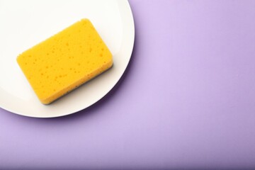 Kitchen sponge and plate on violet background, top view. Space for text