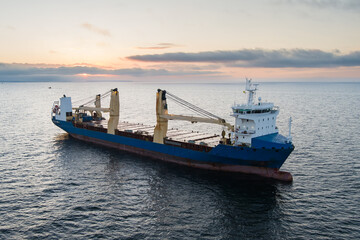 Naklejka premium General cargo ship sailing on the tranquil Baltic Sea near the coast of Estonia at sunrise during a golden hour dawn.