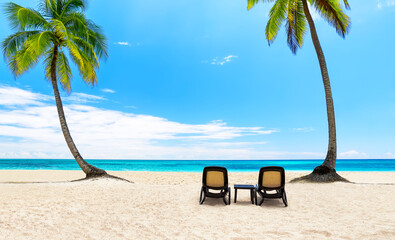 Beach chairs on white sandy beach with coconut palm trees and turquoise sea. Summer beach vacation and travel concept.