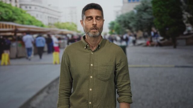 Man points finger to temple on a crowded street market, eyes closed and limp gesture; urban fatigue.