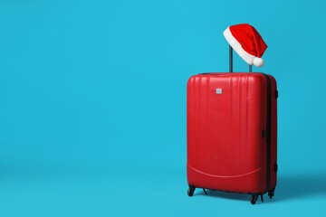 Christmas vacation. Suitcase with red Santa hat on light blue background