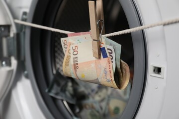 Banknotes hanging on clothesline near washing machine, closeup