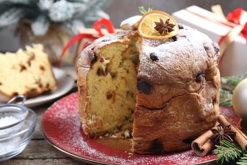 Tasty Christmas panettone cake with powdered sugar and festive decor on wooden table, closeup