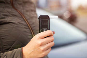 Female Hand Holds Portable Alcometer With Display. Checking Sobriety Next To Automobile. Copy space for text