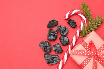 Christmas gift for naughty kids. Pieces of black coal, festive decor and candy cane on red background, flat lay. Space for text