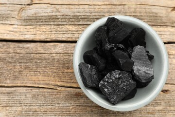 Pieces of black coal in bowl on wooden table, top view. Space for text