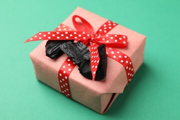 Pieces of black coal and Christmas gift box on green background, closeup
