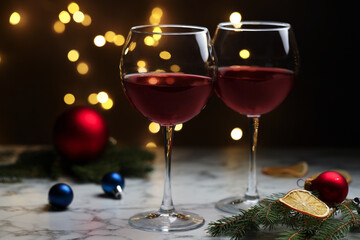 Glasses of red wine and Christmas decor on light marble table against blurred lights