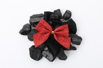 Obraz premium Pieces of black coal with red bow isolated on white, top view. Christmas tradition for kids