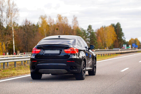 Fototapeta Black luxury sport utility vehicle SUV driving on highway road during autumn season, journey vehicle movement on asphalt way with guardrail and colorful trees under cloudy sky