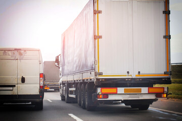 Rear view of truck trailer and delivery van on highway. Road transport and logistics concept during daytime with bright sky