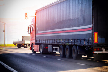 Red heavy cargo truck with dark curtain-side trailer traveling on highway, stopped at red traffic light with countdown