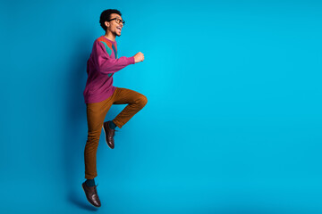 Energetic young man in casual colorful attire jumping against a vivid blue background showcasing joy and vitality