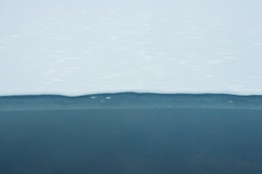 Abstract horizontal texture of a frozen reservoir divided into two parts: white snowy ice on top and blue, open water on the bottom creating a cold and abstract nature background - Powered by Adobe