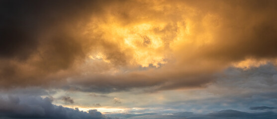 Epic panoramic view golden rain clouds during sunset or sunrise breaking through dark storm clouds creating powerful heavenly background with bright light