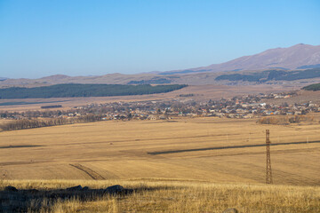 Obraz premium Fields of faded, bright brown grass. Houses in the village of Beshtasheni. Hills, forests, and a bright blue sky in the background.