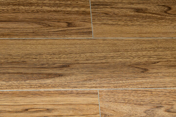 Detailed texture shot of wood-look flooring or tiling, featuring rich, medium-brown tones and defined grain patterns.