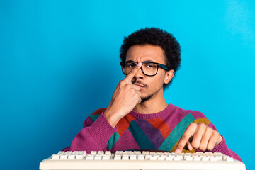 Young man wearing colorful sweater posing with keyboard against blue background, highlighting style and expression