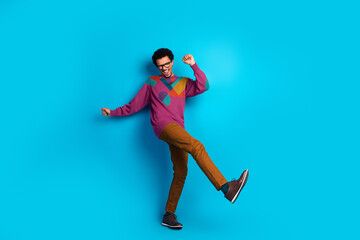 Happy young man in stylish casual outfit dancing against vibrant blue background, showcasing joyful and energetic expression