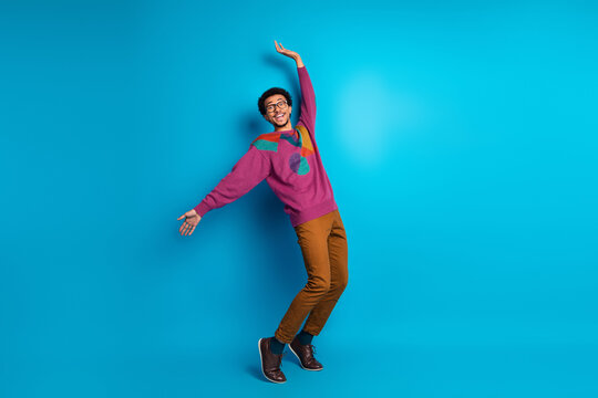 Trendy young man wearing a colorful sweater dancing joyfully against a vibrant blue background, showing lively energy - Powered by Adobe