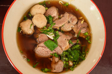 The closed up of Thai noodles. Asian noodle soup with beef meatball with fresh vegetable on wood table. 