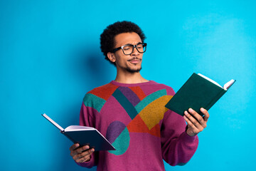 Young man in colorful sweater reading two books against vibrant blue background