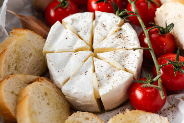 Baked camembert cheese with garlic, cherry tomatoes and baguette bread. Closeup view. Gourmet hot appetizer