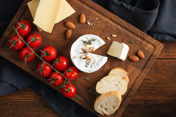 Wooden serving tray with camembert, aged gouda, cherry tomatoes, almonds and baguette