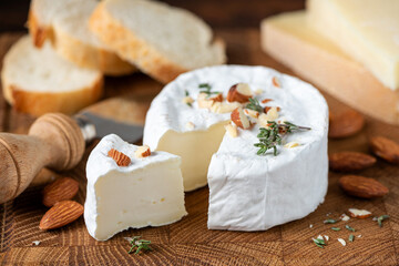 Camembert cheese served with almonds and aged gouda cheese on wooden serving board