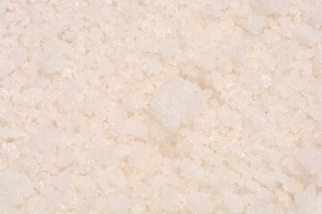 A close-up, high-angle texture shot fills the frame with densely packed, coarse, white and pale pinkish-white natural sea salt crystals