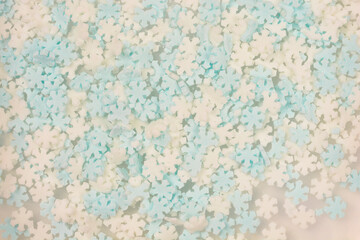 A close-up, overhead shot fills the frame with a textured pattern of small, scattered edible white and light blue sugar snowflake sprinkles