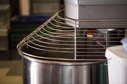 Commercial kitchen mixer featuring large stainless steel bowl and protective metal safety guard, essential equipment for baking and food production closeup shot