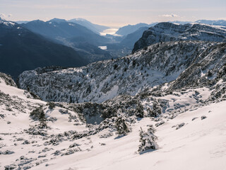 Snowy mountain landscape with a valley and Garda lake in the distance, seen from a high vantage point. Paganella, Roda refuge,Trentino, Italy