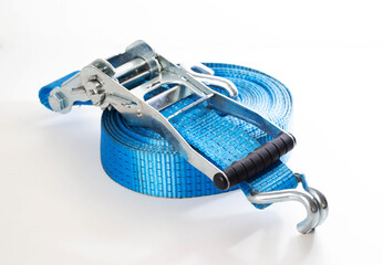 Blue ratchet strap coiled on white background. Heavy duty cargo tie down equipment with metal hooks...