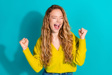 Young woman celebrates in a bright yellow sweater against turquoise background with a joyful smile...