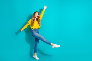 Young woman in bright yellow sweater leaps with joy against a blue background showcasing casual...