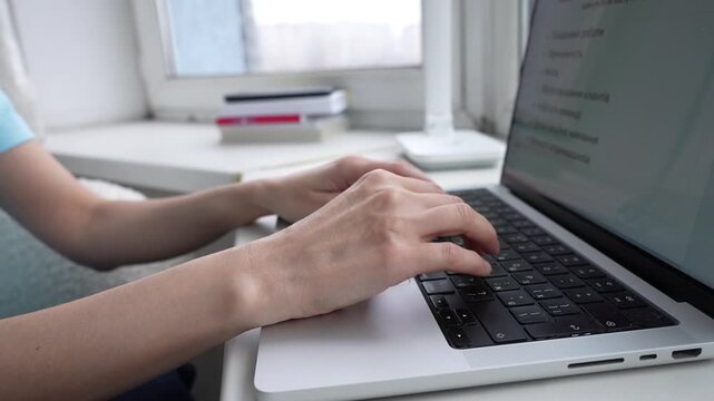 Hands type rapidly on a laptop in a warm, inviting workspace. Sunlight streams through the window, creating a bright atmosphere conducive to creativity.