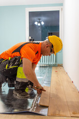 A man is laying wooden flooring. A finishing worker at work. Apartment renovation.