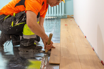 A man is laying wooden flooring. A finishing worker at work. Apartment renovation.