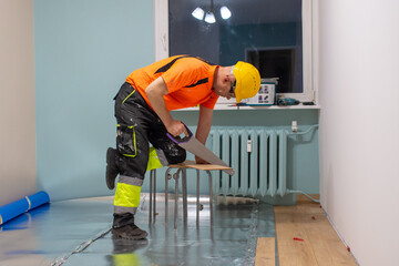 A man is laying wooden flooring. A finishing worker at work. Apartment renovation.