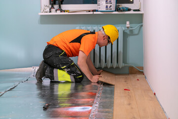 A man is laying wooden flooring. A finishing worker at work. Apartment renovation.