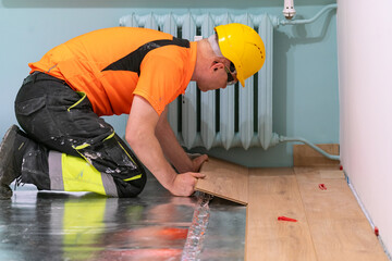 A man is laying wooden flooring. A finishing worker at work. Apartment renovation.